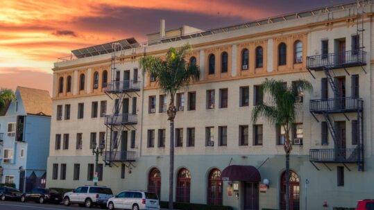 Older Los Angeles apartment building with fire escapes and palm trees at sunset