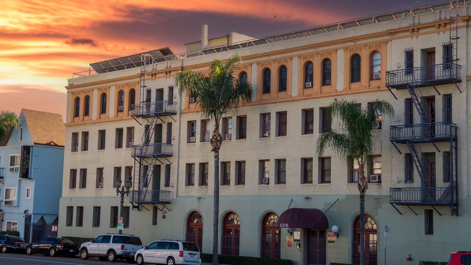 Older Los Angeles apartment building with fire escapes and palm trees at sunset