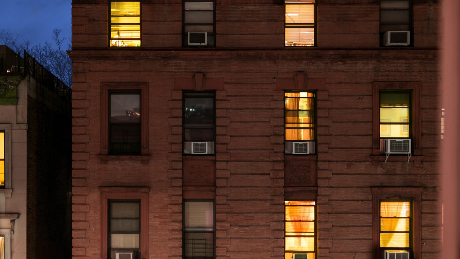New York apartment building at dusk with lit windows and air conditioners