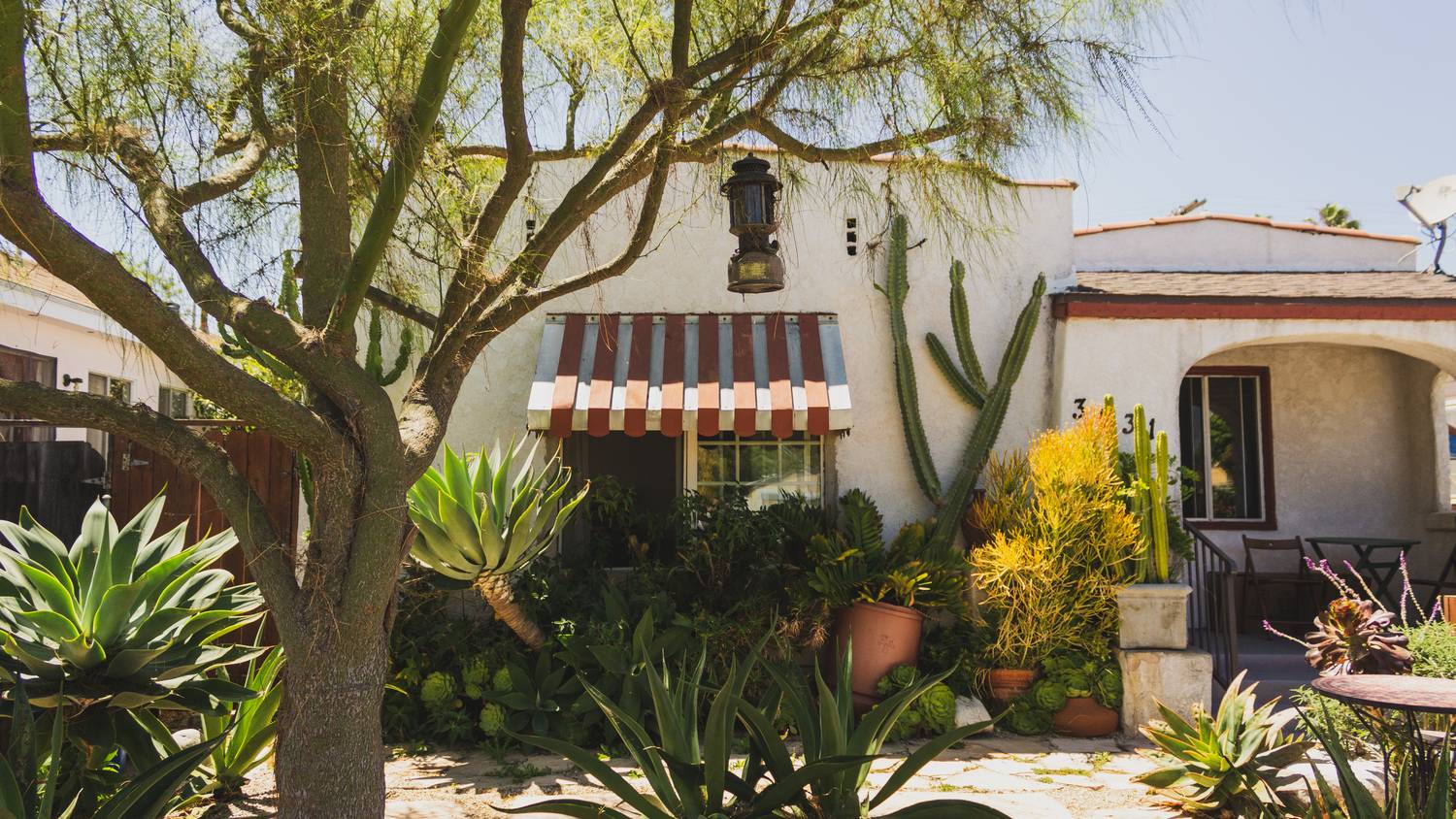 Small Spanish-style California rental bungalow with a striped awning and cactus garden