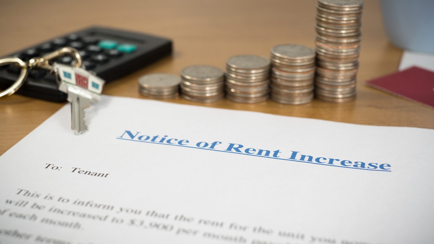 Notice of rent increase letter with house keys, coins and a calculator on a desk